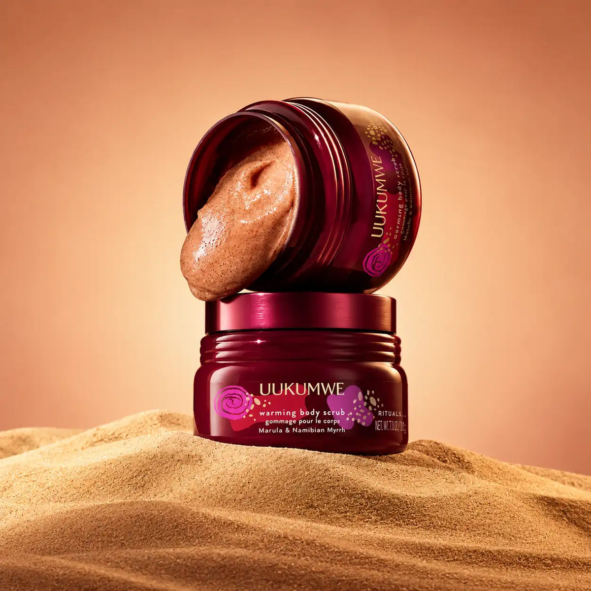 Pot de gommage corporel en bordeaux profond uukumwe, avec une pâte exfoliante texturée couleur beige qui déborde de son couvercle ouvert.
